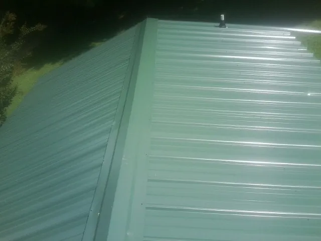 New green metal panels meeting at the ridge of a roof — Flat Roof Repair work by our crew in Farmington